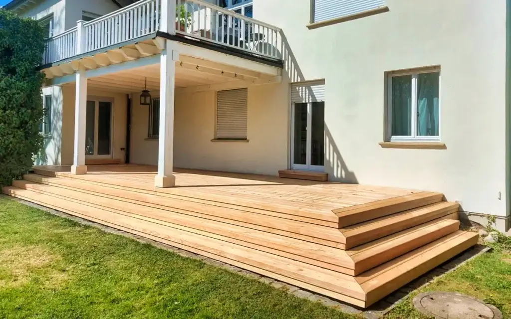 Holzterrasse mit Stufen am Wohnhaus, darüber ein Balkon