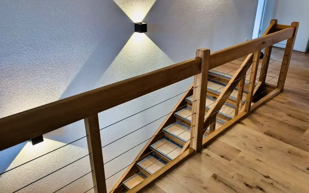 Moderne Holztreppe mit filigranem Geländer und Wandleuchte
